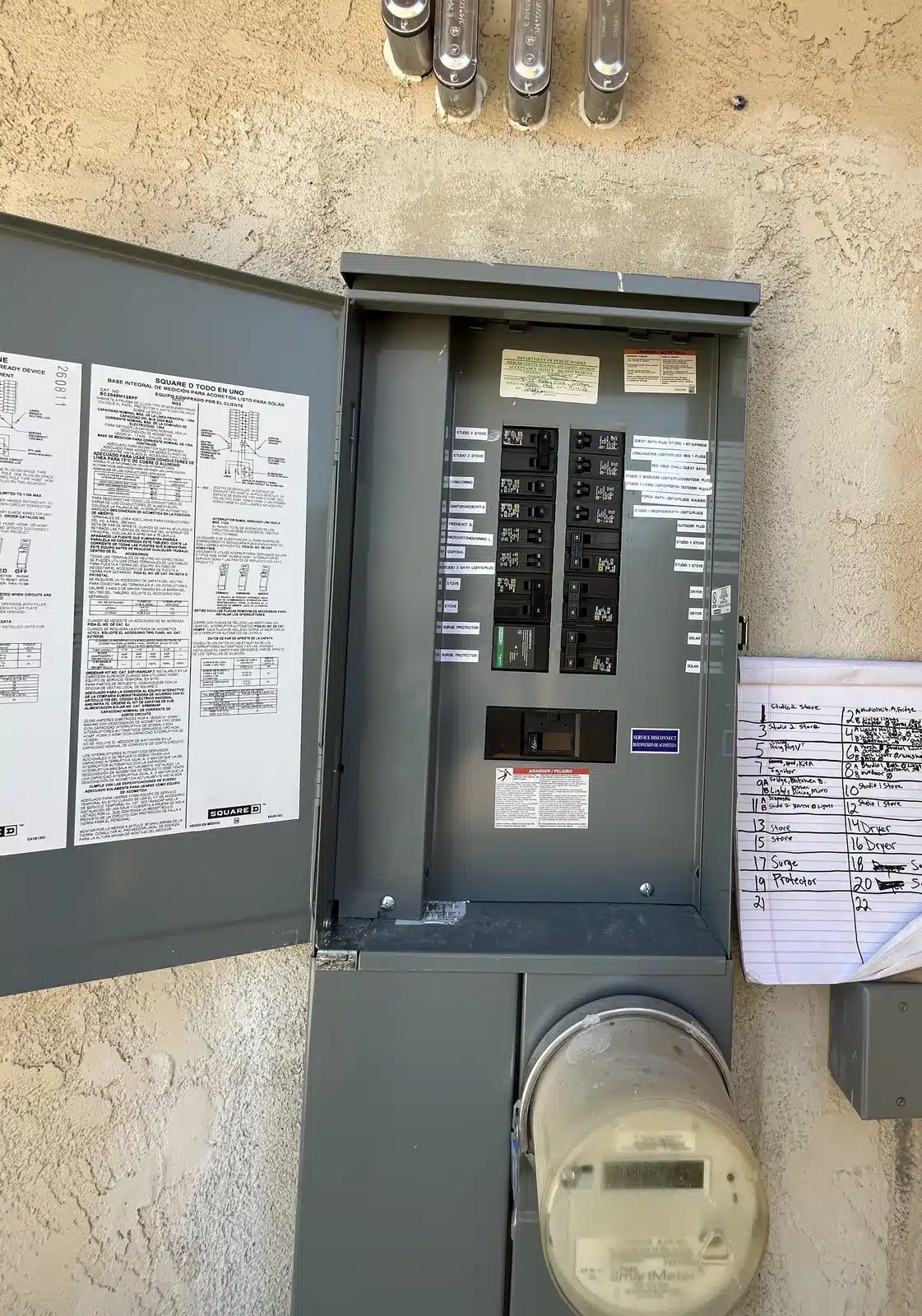 Finished outdoor service panel with door open and breakers installed on a stucco home in Merced County